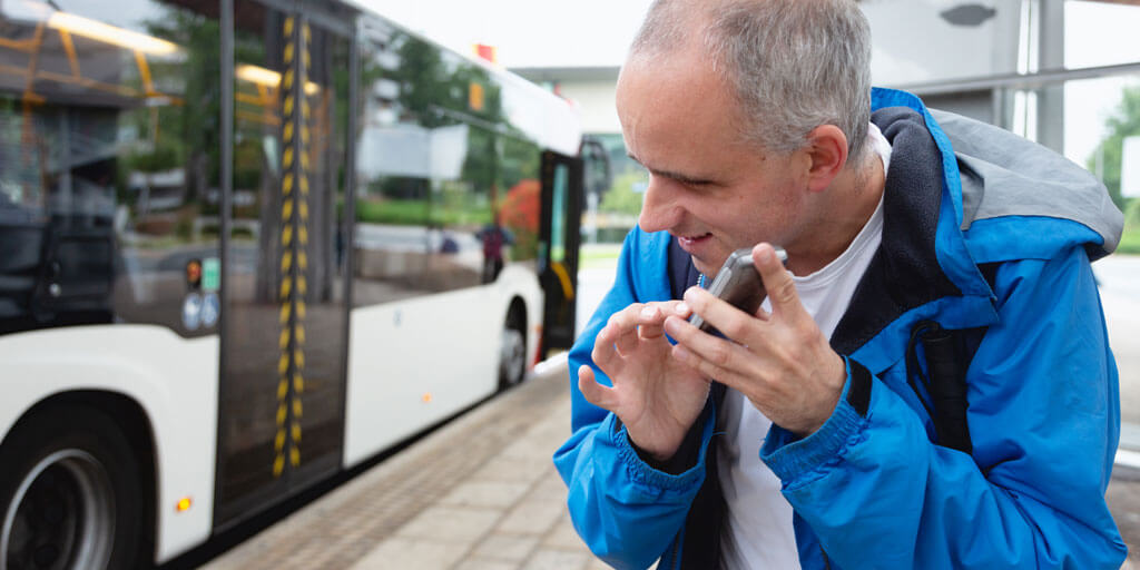 Low-vision man holding a digital device to his ear for bus schedule information