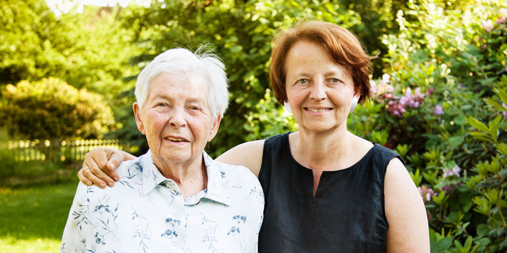 a senior woman standing with her daughter outdoors