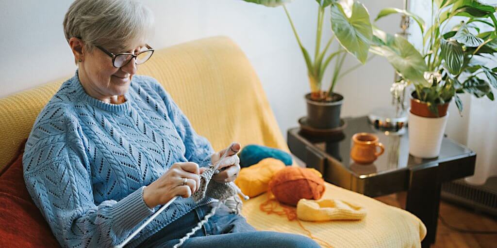 A senior woman with eyeglasses is knitting.