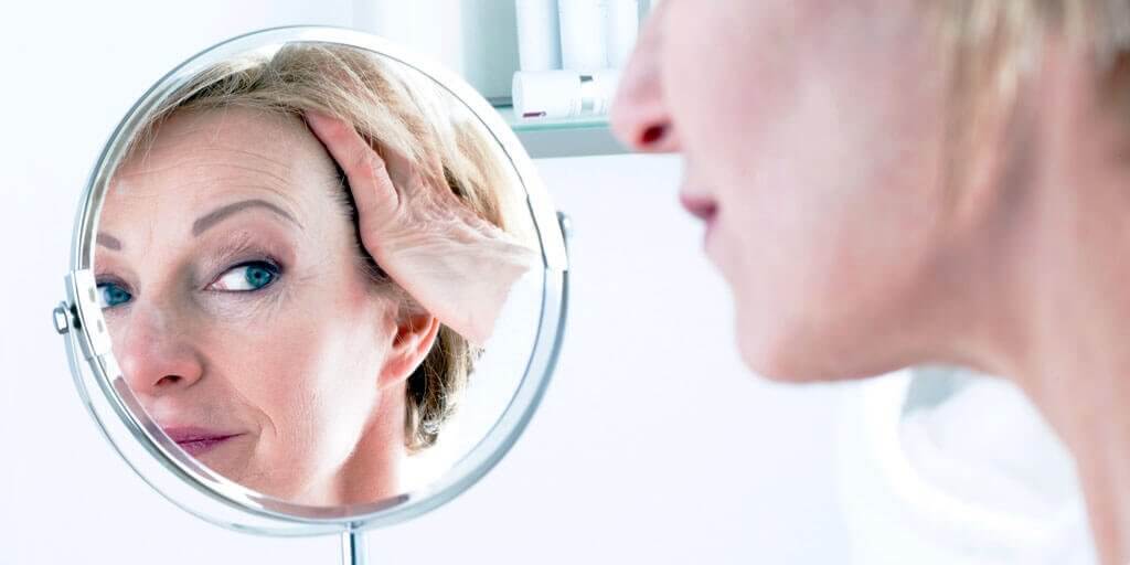 A 40+ woman looking at her face in a mirror.