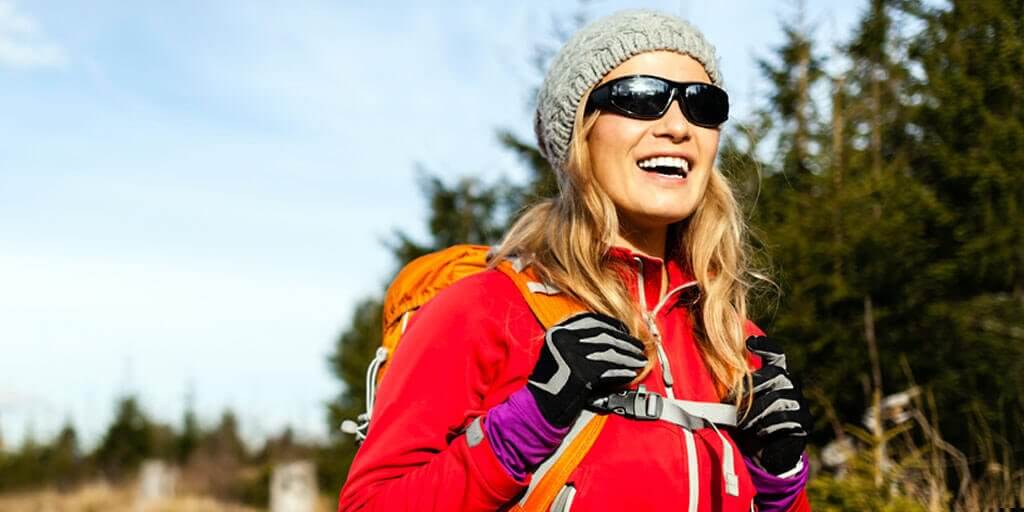 A middle-aged woman wearing sunglasses, hiking outdoors in fall.