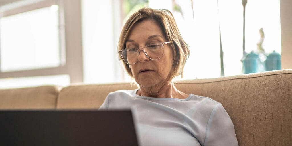 A middle-aged woman wearing eyeglasses using a laptop computer.