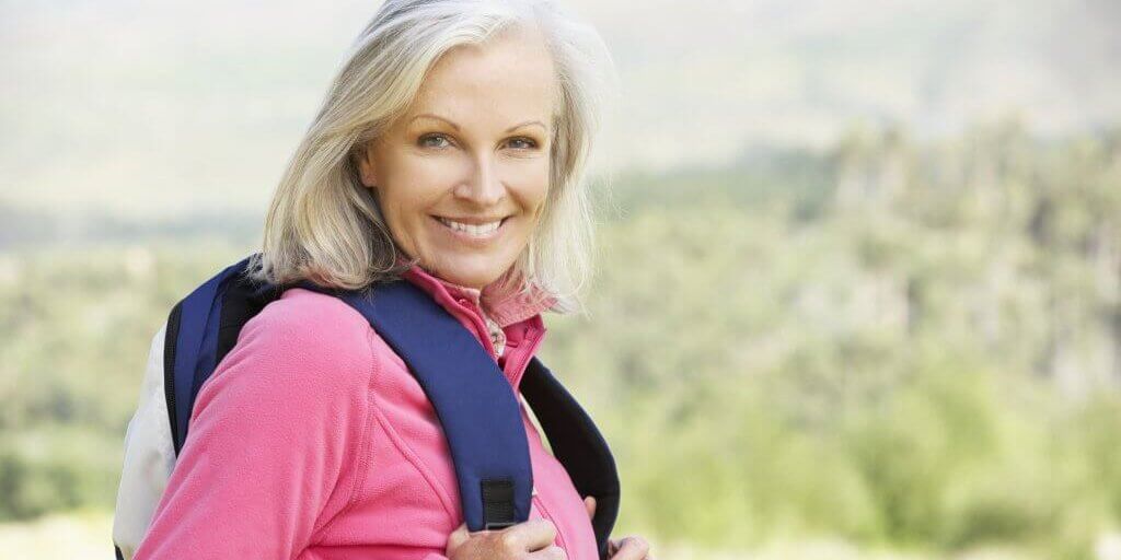 Senior woman in pink jacket carrying a backpack Portrait Of Senior Woman On Hike Smiling At Camera