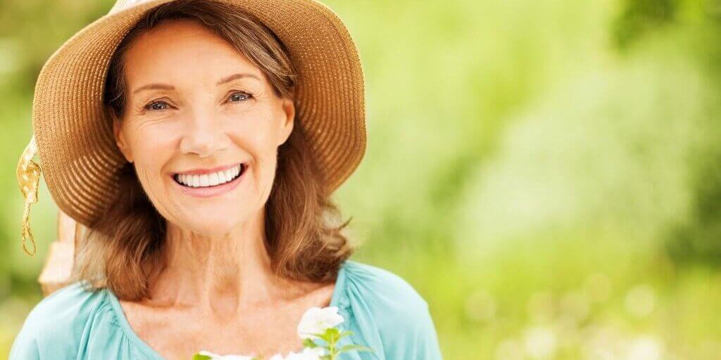 Portrait of happy senior woman in sun hat with flowers in garden. Horizontal shot.