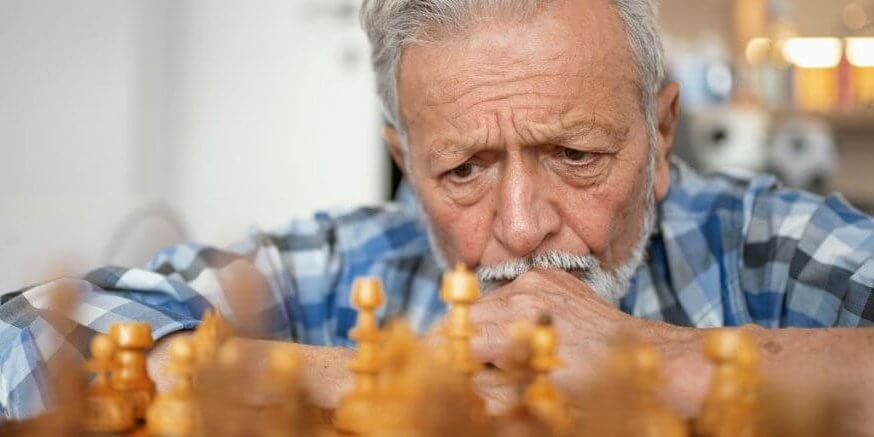 A senior man is thinking about his next chess move.