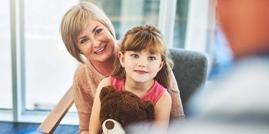 Eine sitzende Mutter und ihre kleine Tochter unterhalten sich mit dem Arzt.